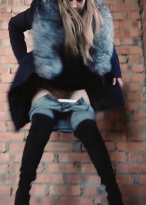 Расстроенная девушка садится на корточки, чтобы пописать на открытом воздухе, одетая в тяжелое зимнее пальто